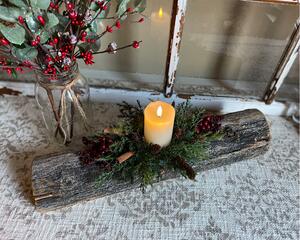 A Christmas yule log candle centerpiece. It is made from upcycled wood with a white candle, greenery, and berries arranged on the top.  